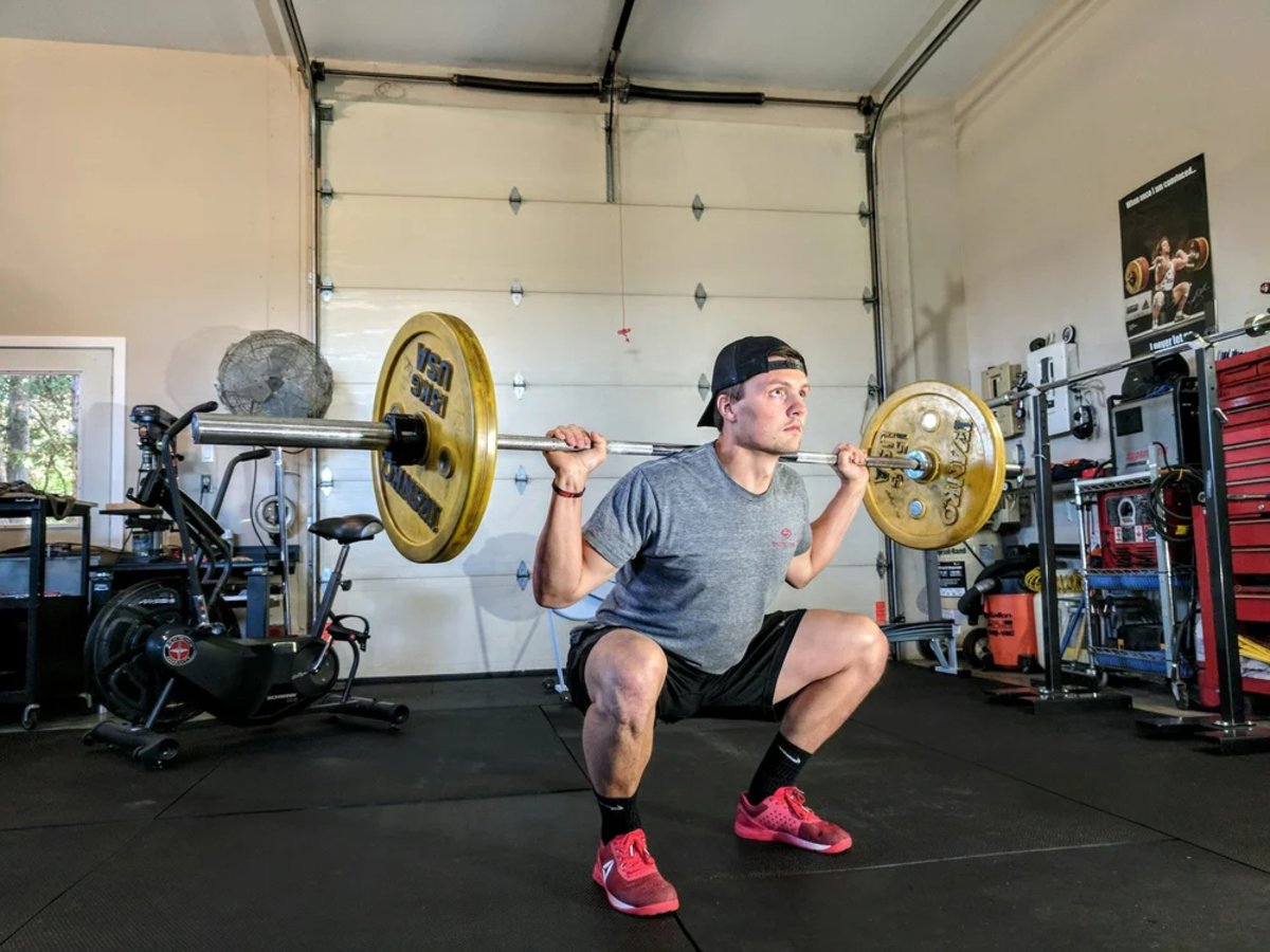 Runner performing a barbell back squat in a garage gym